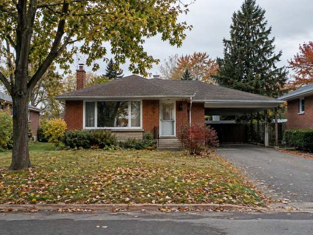 A modest 1950s red-brick bungalow with a carport on a wide Burlington lot, autumn leaves on the lawn