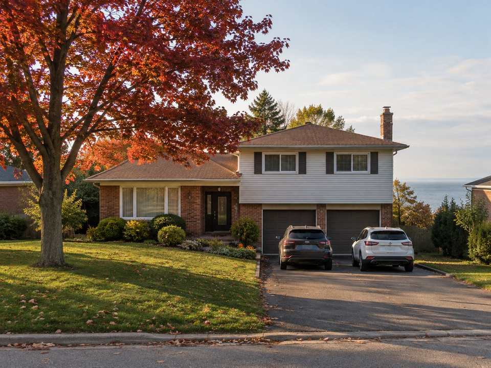 A 1970s brick and siding side-split house with a red maple in the front yard on a quiet Burlington street in October