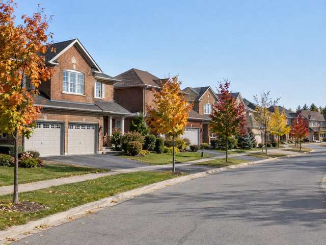 A curving street of 1980s and 1990s two-storey brick houses with double garages and young trees in autumn colour